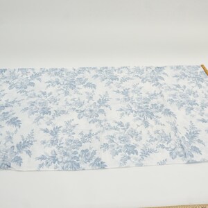 May include: A rectangular piece of fabric with a white background and a blue floral pattern. A wooden ruler is placed along the edge of the fabric. The fabric is likely used for sewing or crafting.