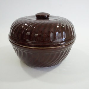 May include: A brown ceramic casserole dish with a lid. The dish has a swirl design and a cream-colored rim.