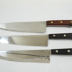May include: Three stainless steel chef knives with different handle designs. The top knife has a wooden handle with brass rivets, the middle knife has a black handle with three rivets, and the bottom knife has a black handle with three rivets.