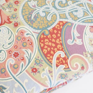 May include: Close-up of a fabric with a detailed paisley pattern. The design features a mix of colors, including light blue, peach, red, yellow, and purple. The fabric has a soft, floral design.