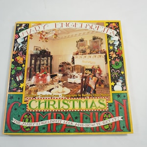 May include: A colorful book titled "Christmas Companion" by Mary Engelbreit. The cover features a festive interior scene with a decorated dining table and fireplace. The book's title is in large, decorative letters, with additional text.