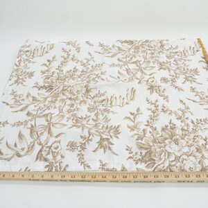 May include: A piece of fabric with a floral pattern in shades of brown and beige. The design features detailed botanical illustrations of flowers and foliage. A wooden ruler with inch measurements is placed along the edge of the fabric.