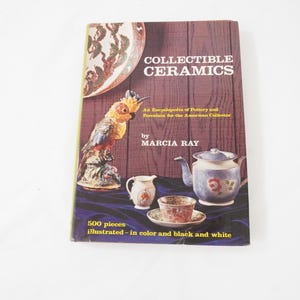 Może przedstawiać: Zabytkowa książka zatytułowana "Collectible Ceramics" z brązową okładką. Na okładce znajduje się kolorowa figurka papugi, czajnik i zestaw filiżanek. Książka jest encyklopedią ceramiki i porcelany dla kolekcjonerów.