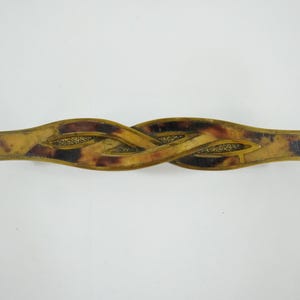 Könnte beinhalten: Vintage Haarspange mit geflochtenem Design. Die Spange hat ein Schildpattmuster in Braun- und Beigetönen, akzentuiert mit goldfarbenem Metall. Die Spange ist etwa 10 cm lang.