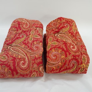 Puede incluir: Dos cojines de sofá acolchados de color rojo con un diseño paisley crema y dorado.