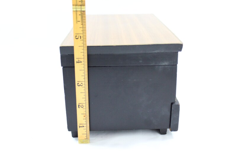 May include: A black wooden box with a woodgrain top and a small drawer. The box is approximately 10 cm tall.