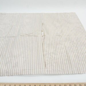 May include: A beige and white striped fabric, likely a pillowcase or similar textile. The fabric has vertical stripes and a seam down the center. The item is laid flat on a white surface.