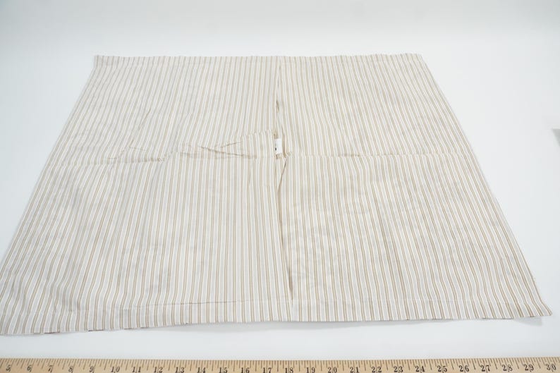 May include: A beige and white striped fabric, likely a pillowcase or similar textile. The fabric has vertical stripes and a seam down the center. The item is laid flat on a white surface.