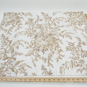 May include: White fabric with a brown floral pattern. A wooden ruler is placed along the edge of the fabric. The fabric features a repeating design of flowers and foliage, creating a classic, elegant look. The ruler measures up to 28 inches.