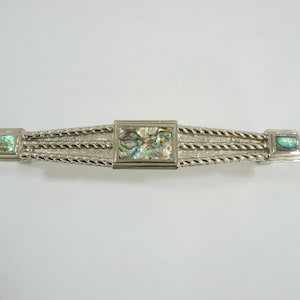 Könnte beinhalten: Silberfarbene Haarklammer mit rechteckigem Abalone-Muschel-Mittelteil und Endstücken. Die Spange hat ein geflochtenes Seil-Design und ist etwa 10 cm lang.