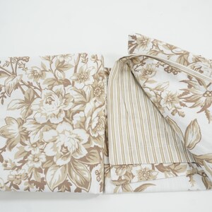 May include: A folded floral fabric with a cream background and large beige flowers and leaves. The reverse side features a beige and white striped pattern. The fabric is likely for bedding or home decor.