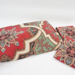 Peut inclure: Un ensemble de literie composé d'une grande housse de couette rectangulaire et de deux taies d'oreiller carrées. Le tissu présente un motif répétitif de médaillons floraux rouges, verts et noirs encadrés par des lignes géométriques crème.
