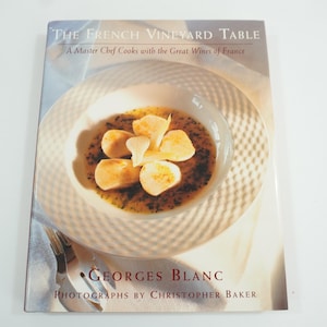 Może przedstawiać: Książka kucharska zatytułowana "The French Vineyard Table: A Master Chef Cooks with the Great Wines of France" autorstwa Georgesa Blanca ze zdjęciem białej miski z białym, kwiatowym daniem.