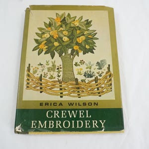 May include: A vintage book titled "Crewel Embroidery" by Erica Wilson. The cover features a tree with yellow fruit, green leaves, and a woven fence. The book has a green and tan color scheme.
