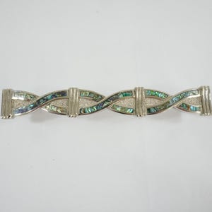 Könnte beinhalten: Silberfarbene Haarspange mit einem verschlungenen Design. Die Haarspange hat Abschnitte aus schillerndem Abalone-Muschel in Grün-, Blau- und Silbertönen. Ein dekoratives Haaraccessoire.