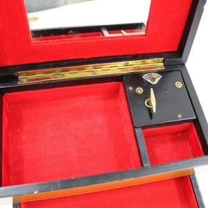 May include: A black wooden music box with a red velvet interior. The box has a hinged lid with a mirror and a winding mechanism on the inside.