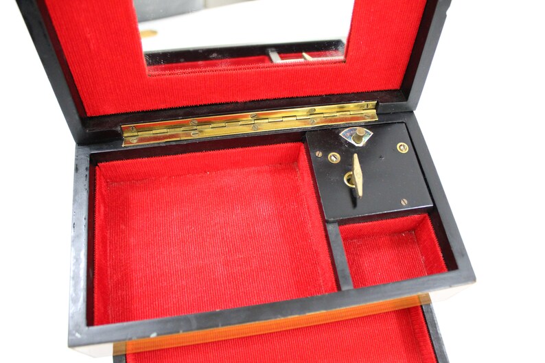 May include: A black wooden music box with a red velvet interior. The box has a hinged lid with a mirror and a winding mechanism on the inside.