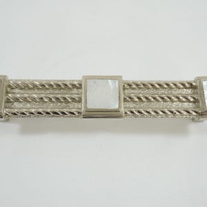 Könnte beinhalten: Silberfarbener Schrankgriff mit Seildesign und quadratischen Perlmutt-Inlays. Der rechteckige Griff ist ca. 15 cm lang und eignet sich für Schubladen oder Schranktüren. Ein dekoratives Hardware-Teil.