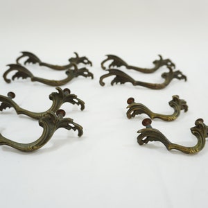 May include: Set of ten antique brass drawer pulls with ornate scrollwork design. Each pull has a decorative, slightly raised, floral pattern.