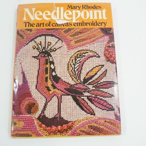 Könnte beinhalten: Ein Buch mit dem Titel "Needlepoint: The art of canvas embroidery" von Mary Rhodes. Der Umschlag zeigt ein farbenfrohes Nadelbild eines stilisierten Vogels mit langem Schwanz.