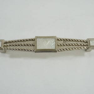 Pode incluir: Puxador de armário prateado com uma incrustação retangular de madrepérola no centro e em cada extremidade. A pega apresenta um design semelhante a uma corda. O hardware é projetado para móveis e armários.