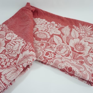 May include: A folded textile featuring a deep red background with a contrasting white floral pattern. The design includes intricate illustrations of various flowers, leaves, and botanical elements, along with a decorative border of repeating motifs.