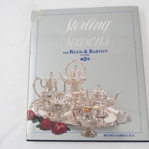 Może przedstawiać: Okładka książki "Sterling Seasons" ze srebrnym serwisem do herbaty. Zestaw do herbaty zawiera imbryki, śmietankę i tacę, z czerwonymi różami na dole. Książka jest autorstwa Renee Garrelick.