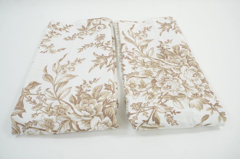 May include: Two folded fabric pieces with a floral pattern. The design features large, detailed flowers and foliage in shades of brown and tan against a white background. The fabric appears to be cotton or a similar material.