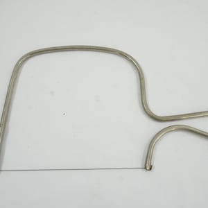 May include: A silver-colored cheese slicer with a wire cutting blade. The slicer has a curved handle and a looped design for easy handling. The wire is stretched between the handle's ends, ready for use.