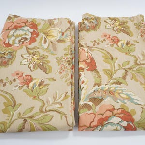 以下が含まれることがあります： 花柄の2つの折り畳まれた布パネル。デザインは、ベージュの背景に、ピーチ、コーラル、クリームの色合いの大きく様式化された花と、緑と茶色の葉が特徴です。生地は中程度の重さのようです。