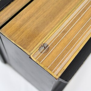 May include: A black wooden box with a gold trim and a wood top with white lines. The box is closed and the top is slightly ajar.