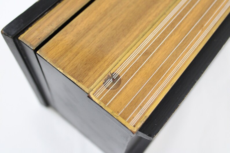 May include: A black wooden box with a gold trim and a wood top with white lines. The box is closed and the top is slightly ajar.