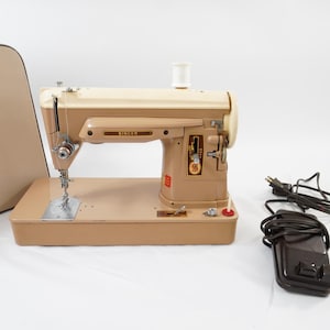May include: A vintage Singer sewing machine in a two-tone beige and cream finish. The machine features a metal needle plate, a top-mounted spool pin, and a control panel with a Singer logo. A dark brown foot pedal with a power cord is included.