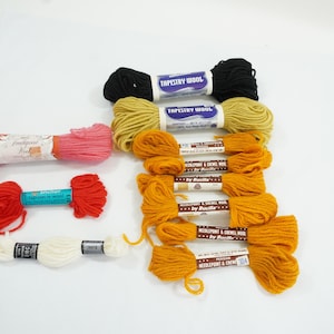 May include: Assortment of colorful yarn skeins, including black, red, white, and yellow. The yarn is labeled "Tapestry Wool" and "Mercerized & Crewel Wool by Bucilla".