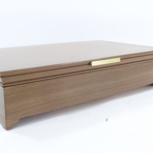 Puede incluir: Una caja de madera con un acabado marrón y una manija de latón en la tapa.