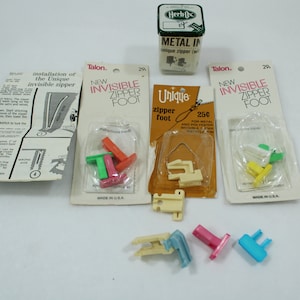 May include: Four packages of sewing machine feet for invisible zippers. The packages are labeled "Talon. New Invisible Zipper Foot" and "Unique zipper foot". The feet are made of white plastic and come in different colors, including green, yellow, orange, pink, and blue.