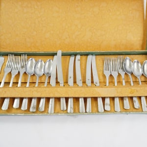 May include: A vintage cutlery set presented in a box. The set includes forks, spoons, knives, and a butter knife. The box is lined with a textured, golden-yellow material and has a green trim. The cutlery is neatly arranged.