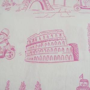 May include: White fabric with a pink illustration of a woman riding a scooter, the Eiffel Tower, and the Colosseum. The design has a travel theme, with other architectural elements and vehicles.