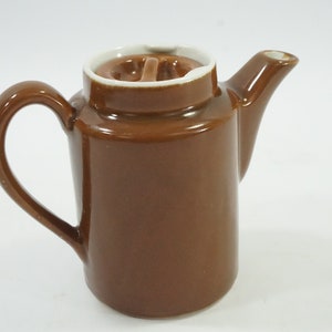 May include: A brown ceramic creamer with a white lid and a handle. The creamer has a simple design and is perfect for serving coffee or tea.