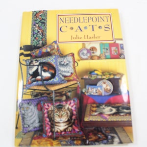 May include: The cover of a book titled "Needlepoint Cats" by Julie Hasler is displayed. The cover is yellow with the title in a decorative font. The image shows needlepoint cat pillows and other cat-themed items.