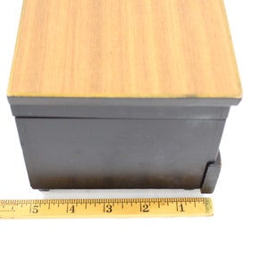 May include: A small wooden box with a black base and a light wood top. The box is 10 cm long and has a drawer on the front.