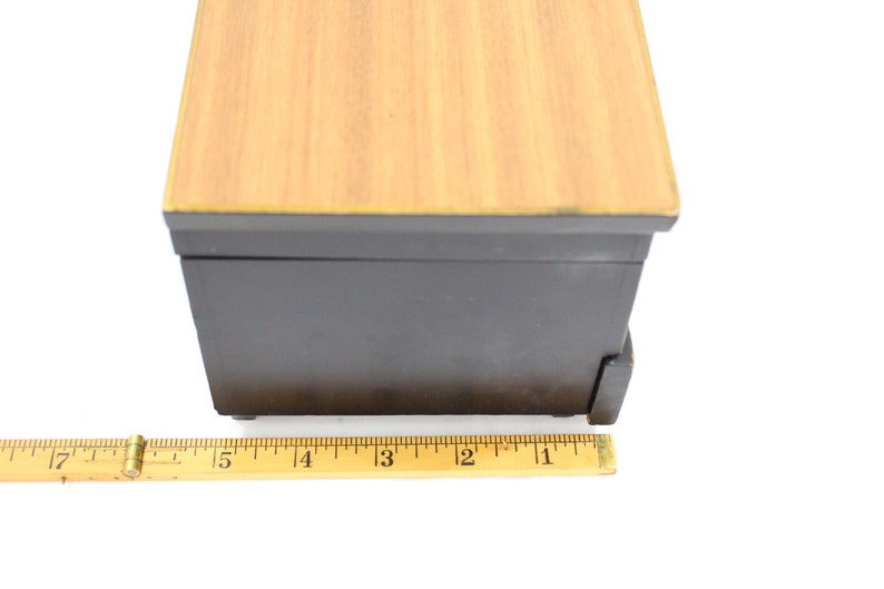 May include: A small wooden box with a black base and a light wood top. The box is 10 cm long and has a drawer on the front.