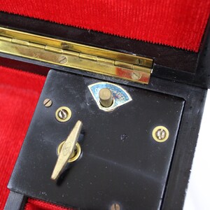 May include: Close-up of a black music box with a brass winding key and a brass knob labelled "On/Off". The music box is open and has a red velvet lining.