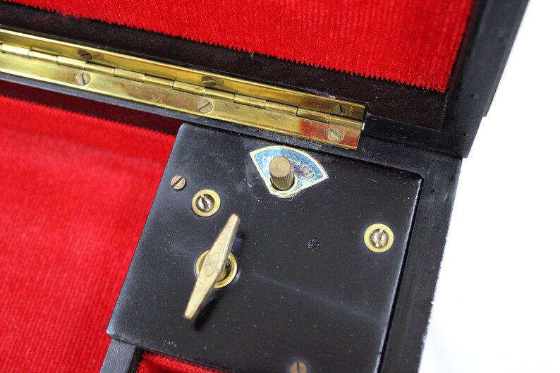May include: Close-up of a black music box with a brass winding key and a brass knob labelled "On/Off". The music box is open and has a red velvet lining.