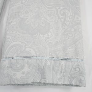 Op de afbeelding: Een lichtgrijze stoffen mouw met een ton-sur-ton paisley-patroon. De manchet is afgewerkt met een fijne rij ajourstiksels die het hoofdgedeelte van de mouw scheidt van de gezoomde rand van de manchet.