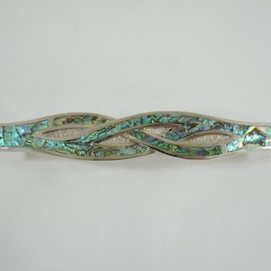 Könnte beinhalten: Silberfarbene Haarspange mit einem verschlungenen Design. Die Haarspange ist mit schillernden Abalone-Muschelteilen in Blau-, Grün- und Silbertönen eingelegt. Dekoratives Haaraccessoire.