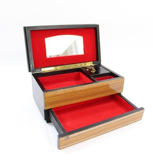 May include: A wooden jewellery box with a red velvet interior. The box has a hinged lid with a mirror and a pull-out drawer. The box is made of wood with a dark brown finish.