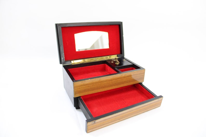 May include: A wooden jewellery box with a red velvet interior. The box has a hinged lid with a mirror and a pull-out drawer. The box is made of wood with a dark brown finish.