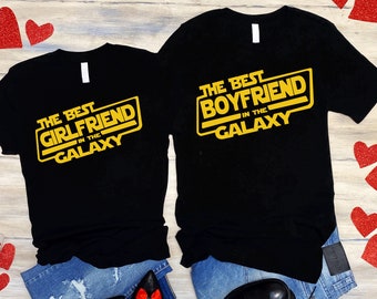 Puede incluir: Dos camisetas negras con un diseño inspirado en Star Wars. El texto en las camisetas dice "The Best Girlfriend in the Galaxy" y "The Best Boyfriend in the Galaxy".