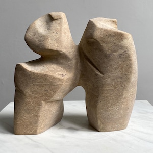 Könnte beinhalten: Abstrakte Skulptur aus hellem braunem Stein. Die Skulptur besteht aus zwei Figuren, die übereinander stehen. Die Figuren sind stilisiert und haben eine raue, strukturierte Oberfläche.